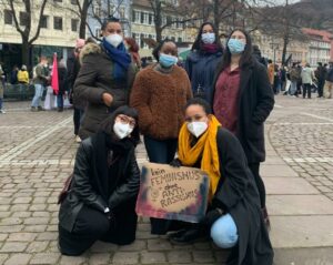 Die Teilnehmer:innen der Demonstration am 8. März stehen mit einem Schild auf dem Marktplatz der Universität Heidelberg und schauen in die Kamera.